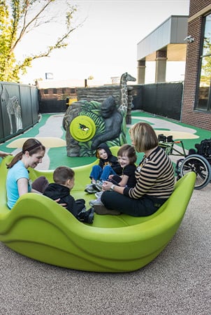Children and adults sit in a lime green OmniSpin Spinner, a playful component that promotes playground accessibility 